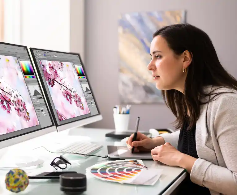 Das Bild zeigt eine Grafikerin bei der Arbeit am PC und mit einem Farbfächer